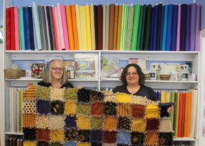 Jeana Paglialunga and her mother, Joyce, hold up a quilt that was made in their shop.