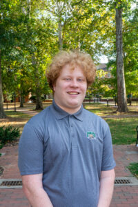 Brandt is standing in front of The Class Gateway, smiling. He is wearing a grey OHIO polo.